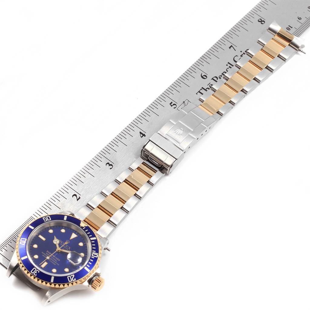 The image shows a Rolex Submariner 16613 Men's Steel and Gold (two tone) Blue Dial 16613 Men's Steel and Gold (two tone) Blue Dial watch laid flat, with its band alongside a ruler for size reference.