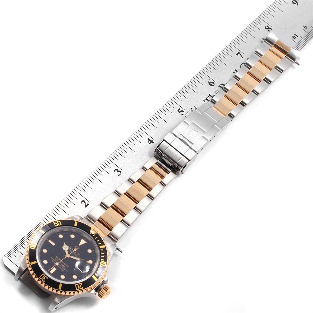 The image shows a top-down view of a Rolex Submariner 16613 Men's Steel and Gold (two tone) Black Dial 16613 Men's Steel and Gold (two tone) Black Dial watch, displaying its face, bezel, bracelet, and clasp placed next to a ruler.