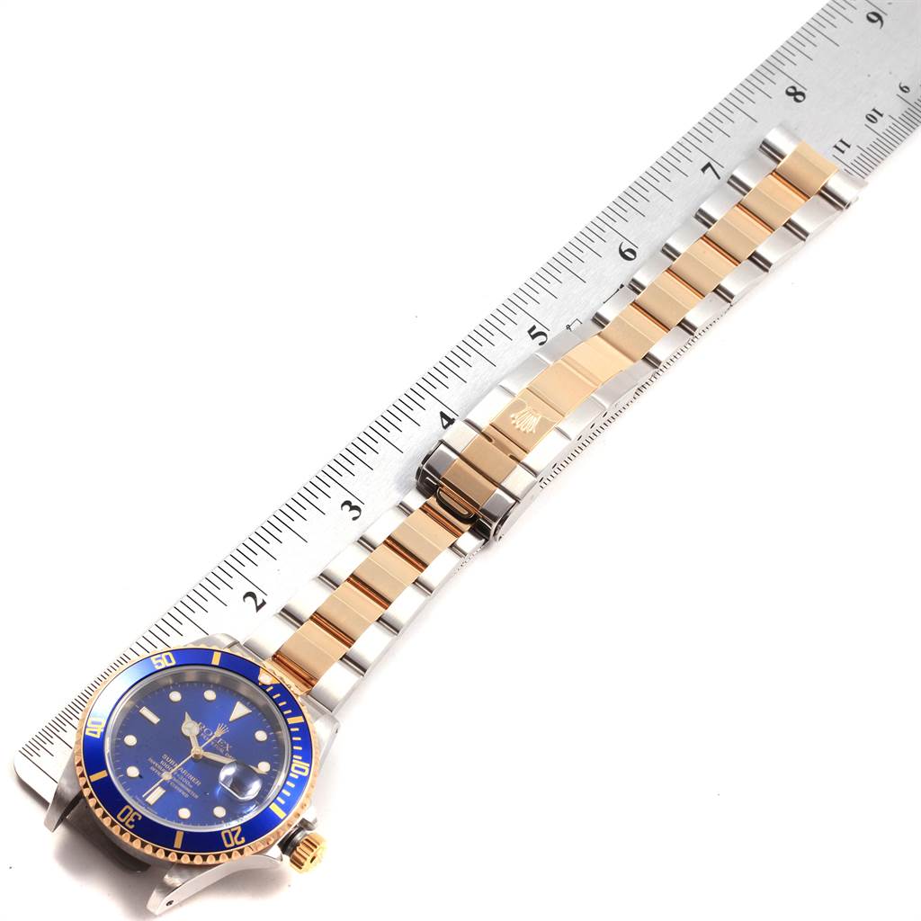 The image shows a Rolex Submariner 16613 Men's Steel and Gold (two tone) Blue Dial 16613 Men's Steel and Gold (two tone) Blue Dial watch laid flat, highlighting the blue dial, bezel, and two-tone bracelet next to a ruler for scale.