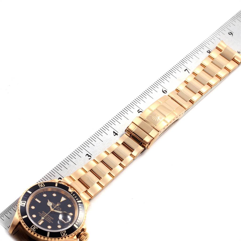 The image shows a Rolex Submariner 16618 Men's Yellow Gold Black Dial 16618 Men's Yellow Gold Black Dial watch, showcasing its black dial, bezel, and gold bracelet, measured alongside a ruler.