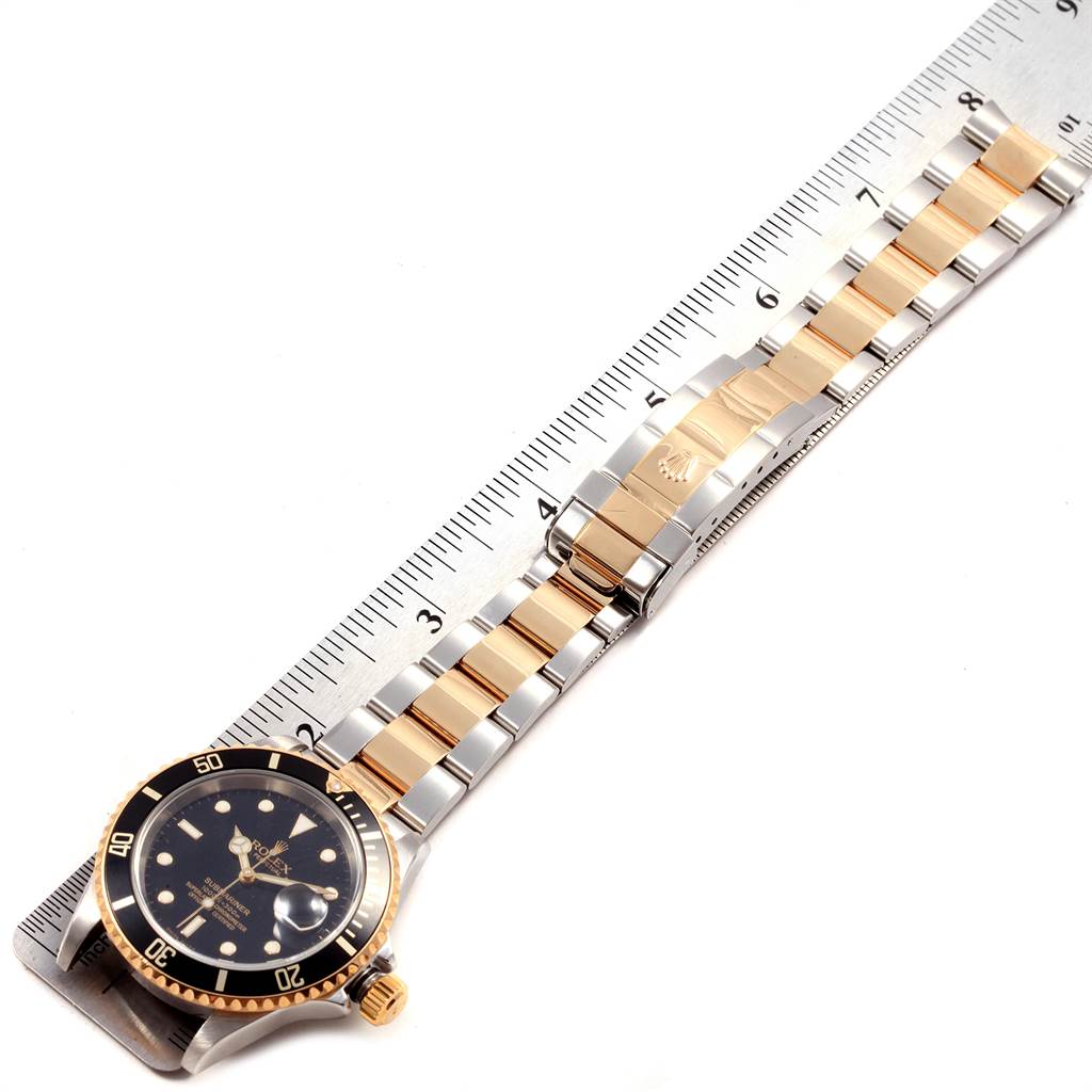 The image shows a top-down view of the Rolex Submariner 16613 Men's Steel and Gold (two tone) Black Dial 16613 Men's Steel and Gold (two tone) Black Dial watch, highlighting its face, band, and clasp placed next to a ruler.