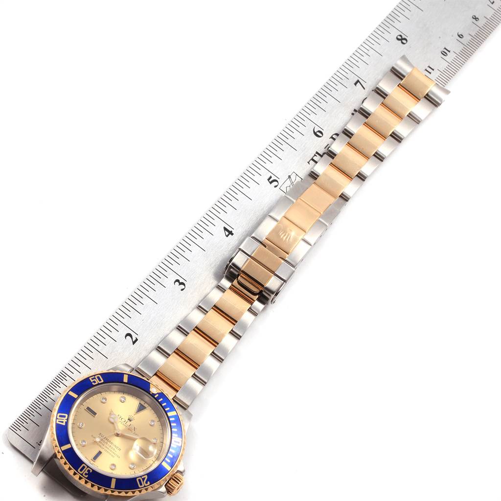 The image shows the Rolex Submariner 16613 Men's Steel and Gold (two tone) Champagne Dial 16613 Men's Steel and Gold (two tone) Champagne Dial watch laid flat with its bezel, dial, and bracelet visible, alongside a measuring ruler.