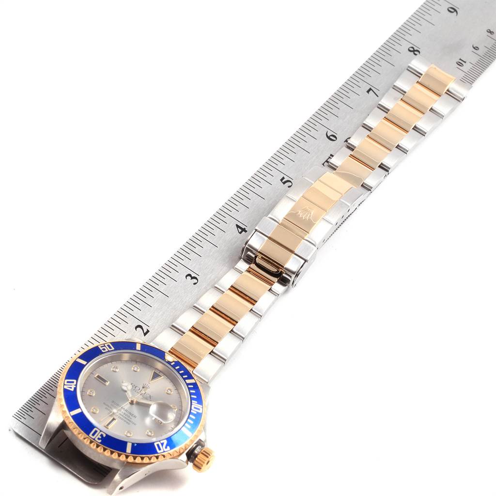 The image shows a Rolex Submariner 16613 Men's Steel and Gold (two tone) Grey Dial 16613 Men's Steel and Gold (two tone) Grey Dial watch lying flat with its face, bezel, band, and clasp visible, next to a ruler for scale.