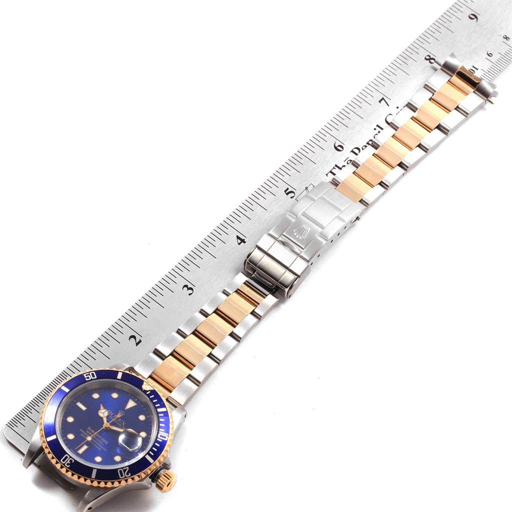 The image shows a full side view of a Rolex Submariner 16613 Men's Steel and Gold (two tone) Blue Dial 16613 Men's Steel and Gold (two tone) Blue Dial model watch, including the face, bracelet, and clasp, next to a ruler for measurement.