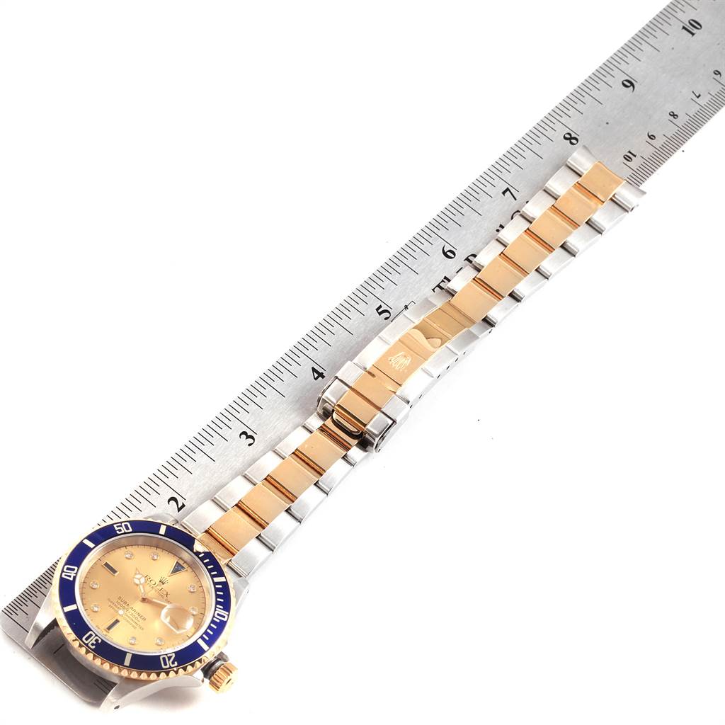 The image shows a Rolex Submariner 16613 Men
s Steel and Gold (two tone) Champagne Dial 16613 Men
s Steel and Gold (two tone) Champagne Dial watch laid flat next to a ruler, displaying the face, bezel, and full bracelet.