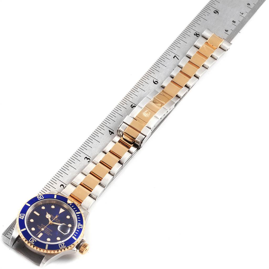 The image shows a top-down view of a Rolex Submariner 16613 Men's Steel and Gold (two tone) Blue Dial 16613 Men's Steel and Gold (two tone) Blue Dial watch with its full bracelet laid out alongside a ruler.