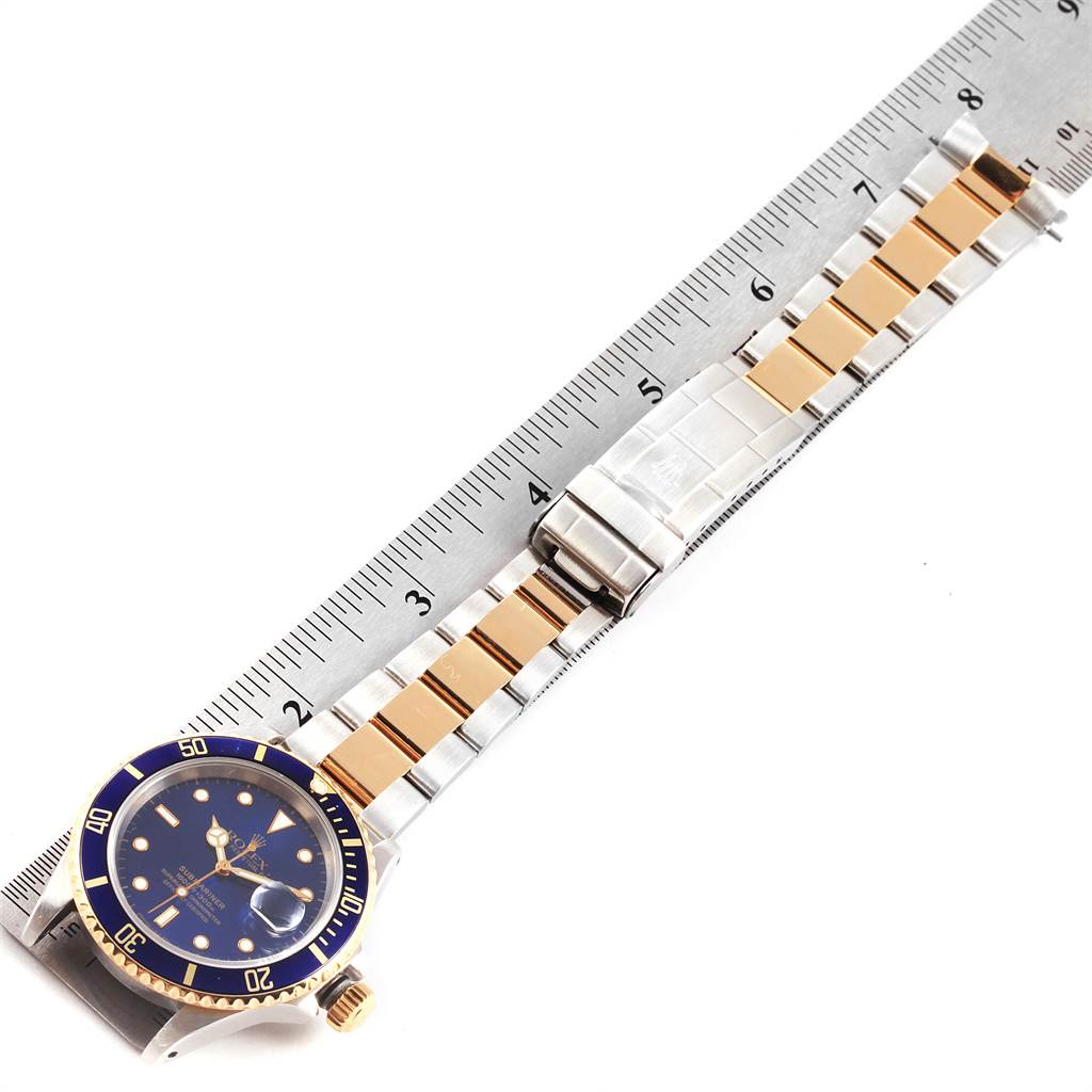 The image shows a top-down view of a Rolex Submariner 16613 Men's Steel and Gold (two tone) Blue Dial 16613 Men's Steel and Gold (two tone) Blue Dial watch with a two-tone metal bracelet placed next to a measuring ruler.