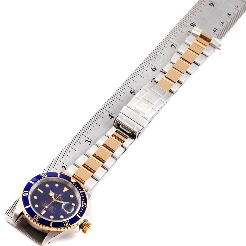 The image shows a Rolex Submariner 16613 Men's Steel and Gold (two tone) Blue Dial 16613 Men's Steel and Gold (two tone) Blue Dial watch lying flat with its band stretched alongside a ruler.