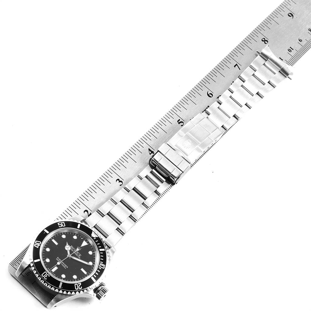 This image shows an overhead shot of a Rolex Submariner 14060 Men's Stainless Steel Black Dial 14060 Men's Stainless Steel Black Dial watch, with its face and bracelet laid out on a ruler.