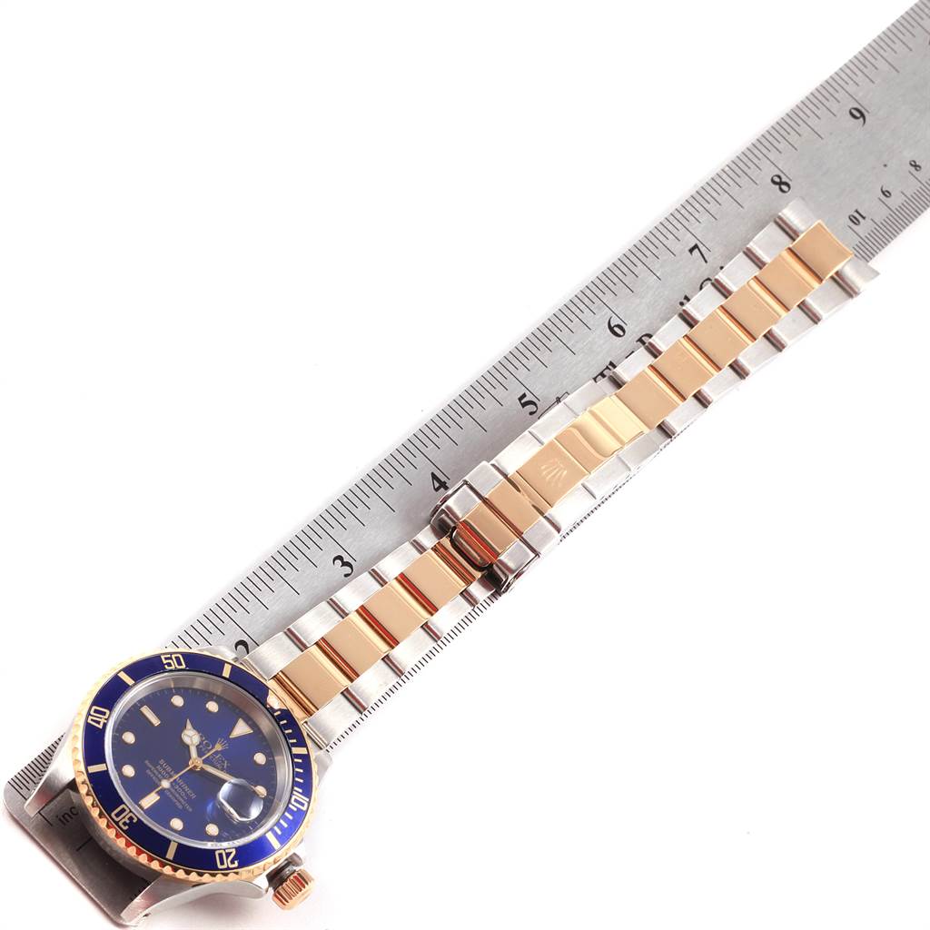 This photo shows a top view of a Rolex Submariner 16613 Men's Steel and Gold (two tone) Blue Dial 16613 Men's Steel and Gold (two tone) Blue Dial watch, highlighting its blue dial, gold bezel, and a portion of the bracelet next to a ruler.