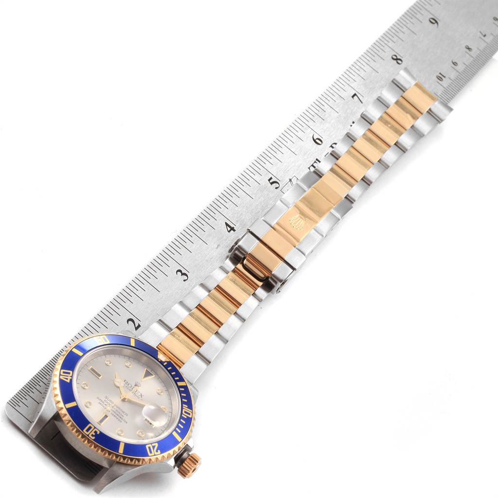 The image shows a top-down view of a Rolex Submariner 16613 Men
s Steel and Gold (two tone) Grey Dial 16613 Men
s Steel and Gold (two tone) Grey Dial watch, its bracelet, and part of a ruler alongside it.