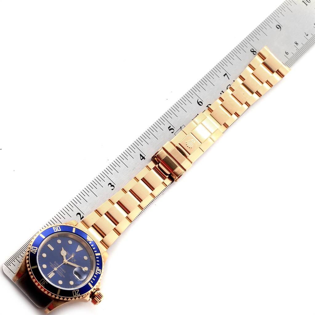 This image displays a Rolex Submariner 16618 Men
s Yellow Gold Blue Dial 16618 Men
s Yellow Gold Blue Dial watch with a blue dial and gold bracelet, aligned next to a ruler.