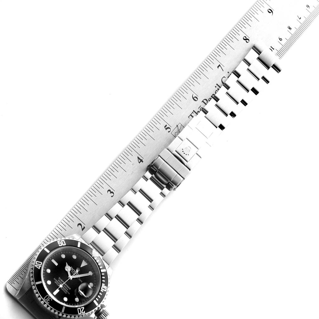 The image shows a Rolex Submariner 16610 Men
s Stainless Steel Black Dial 16610 Men
s Stainless Steel Black Dial watch laid flat with a ruler measuring its length, displaying the bracelet and face.