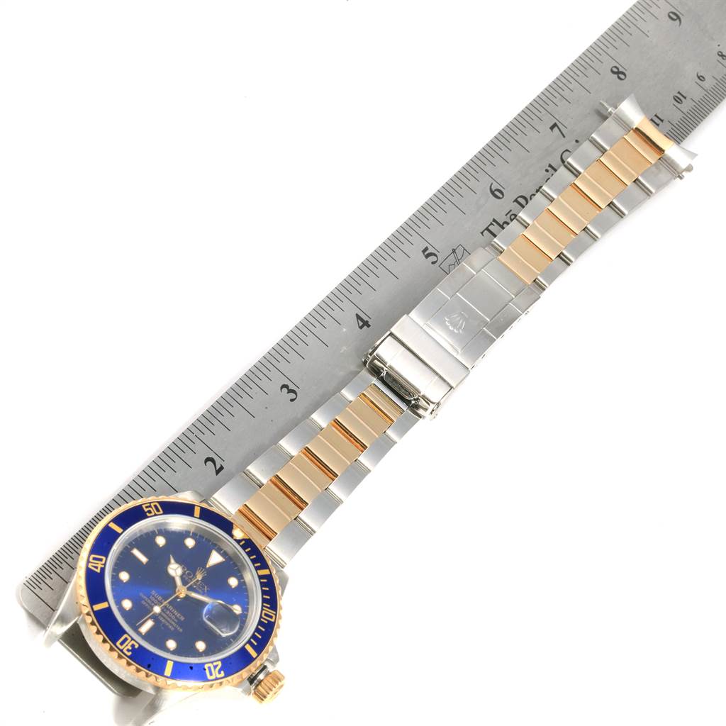 The Rolex Submariner 16803 Men
s Steel and Gold (two tone) Blue Dial 16803 Men
s Steel and Gold (two tone) Blue Dial watch is shown from a top-down angle with the face, bezel, and full bracelet visible next to a ruler.