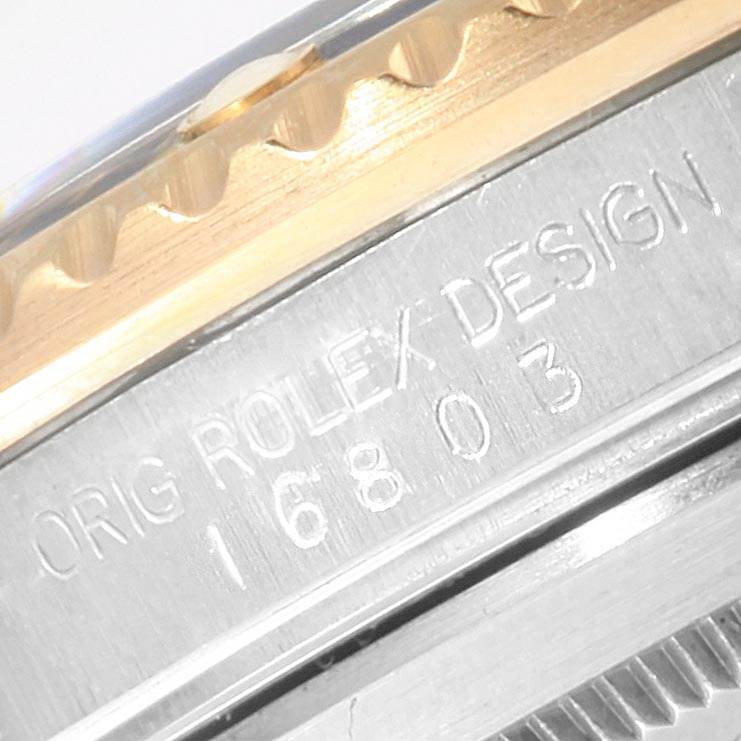 The image shows a close-up of the side of a Rolex Submariner 16803 Men
s Steel and Gold (two tone) Blue Dial 16803 Men
s Steel and Gold (two tone) Blue Dial model 16803, highlighting the engraved text and bezel.