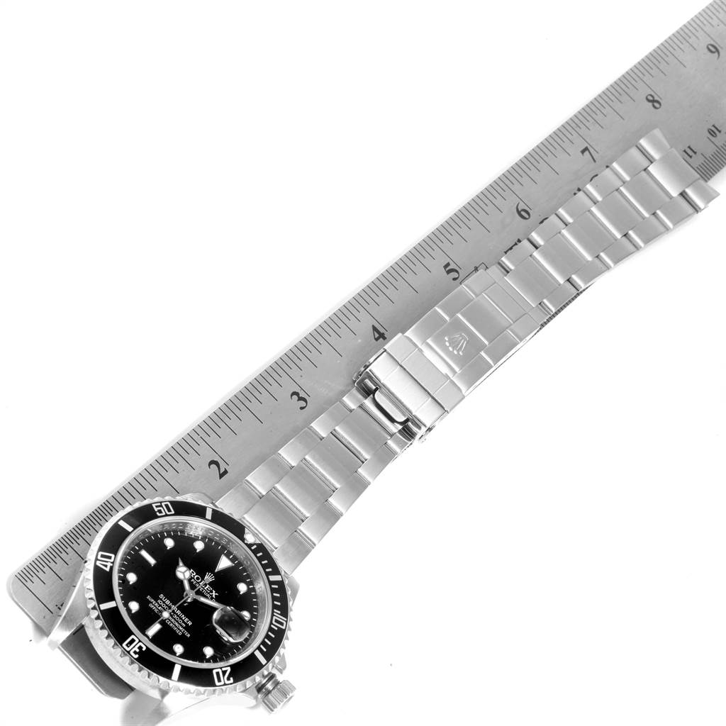 The Rolex Submariner 16610 Men
s Stainless Steel Black Dial 16610 Men
s Stainless Steel Black Dial is shown laid flat with a ruler for scale, displaying the face, bezel, and metal bracelet.