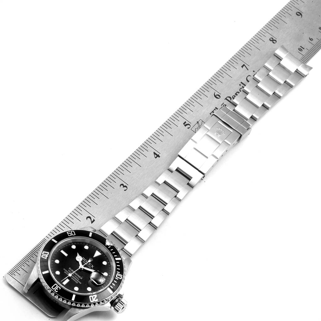 This Submariner model by Rolex is shown vertically next to a ruler, displaying its face and bracelet.