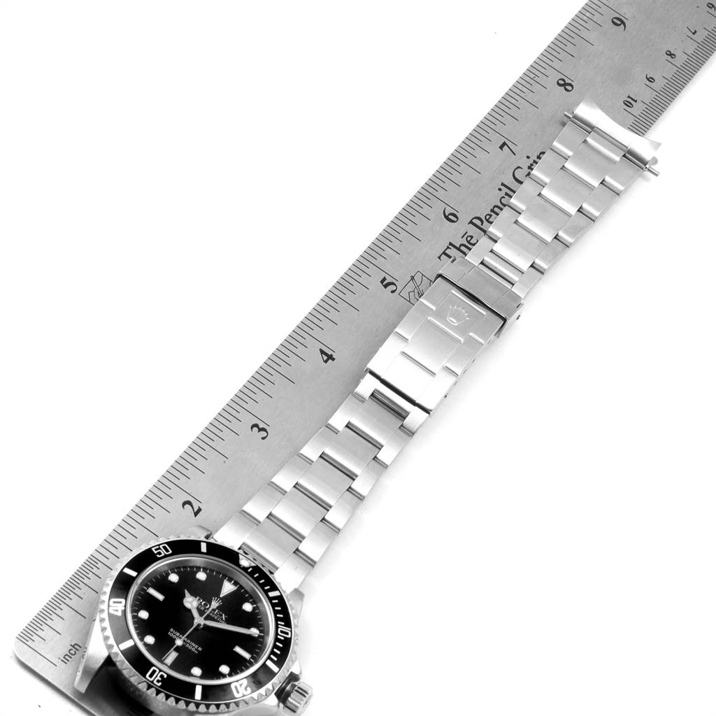 The Rolex Submariner 14060 Men
s Stainless Steel Black Dial 14060 Men
s Stainless Steel Black Dial watch is shown lying flat with a metal ruler, displaying the watch face, bracelet, and clasp.