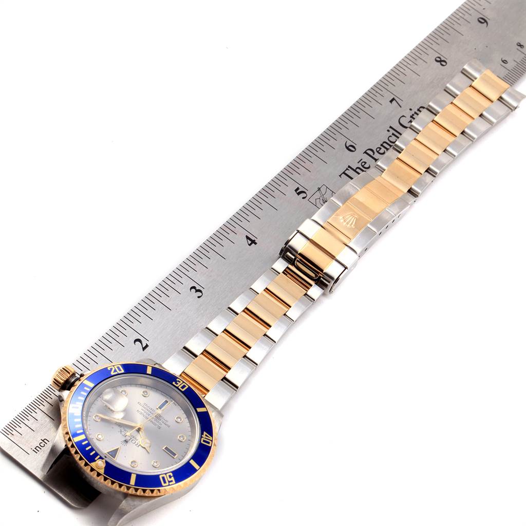 This image shows a top view of a Rolex Submariner 16613 Men
s Steel and Gold (two tone) Grey Dial 16613 Men
s Steel and Gold (two tone) Grey Dial watch and its bracelet alongside a ruler for scale.