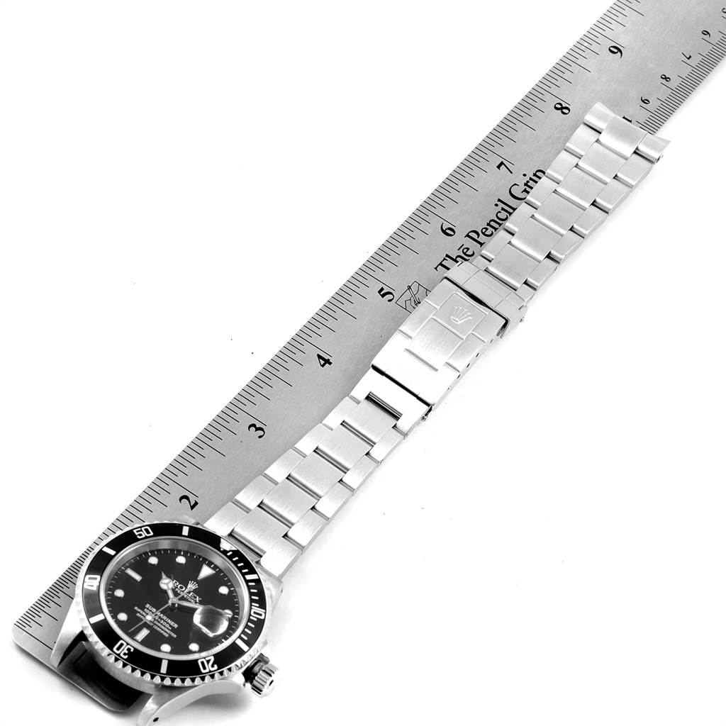 The image displays a Rolex Submariner 16610 Men
s Stainless Steel Black Dial 16610 Men
s Stainless Steel Black Dial watch laying flat with a ruler beside it for measurement.