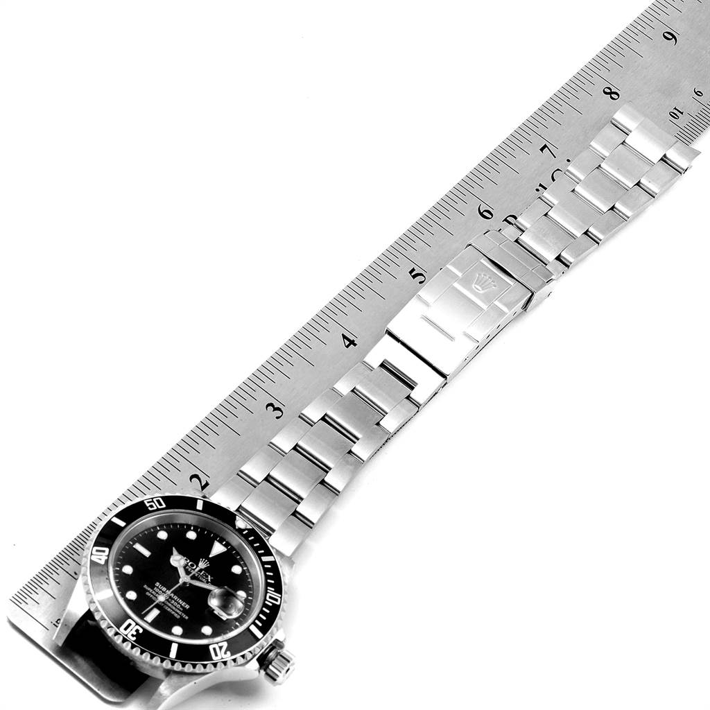 The image shows a side angle of a Rolex Submariner 16610 Men
s Stainless Steel Black Dial 16610 Men
s Stainless Steel Black Dial watch, including the face, bezel, bracelet, clasp, and a ruler for scale.