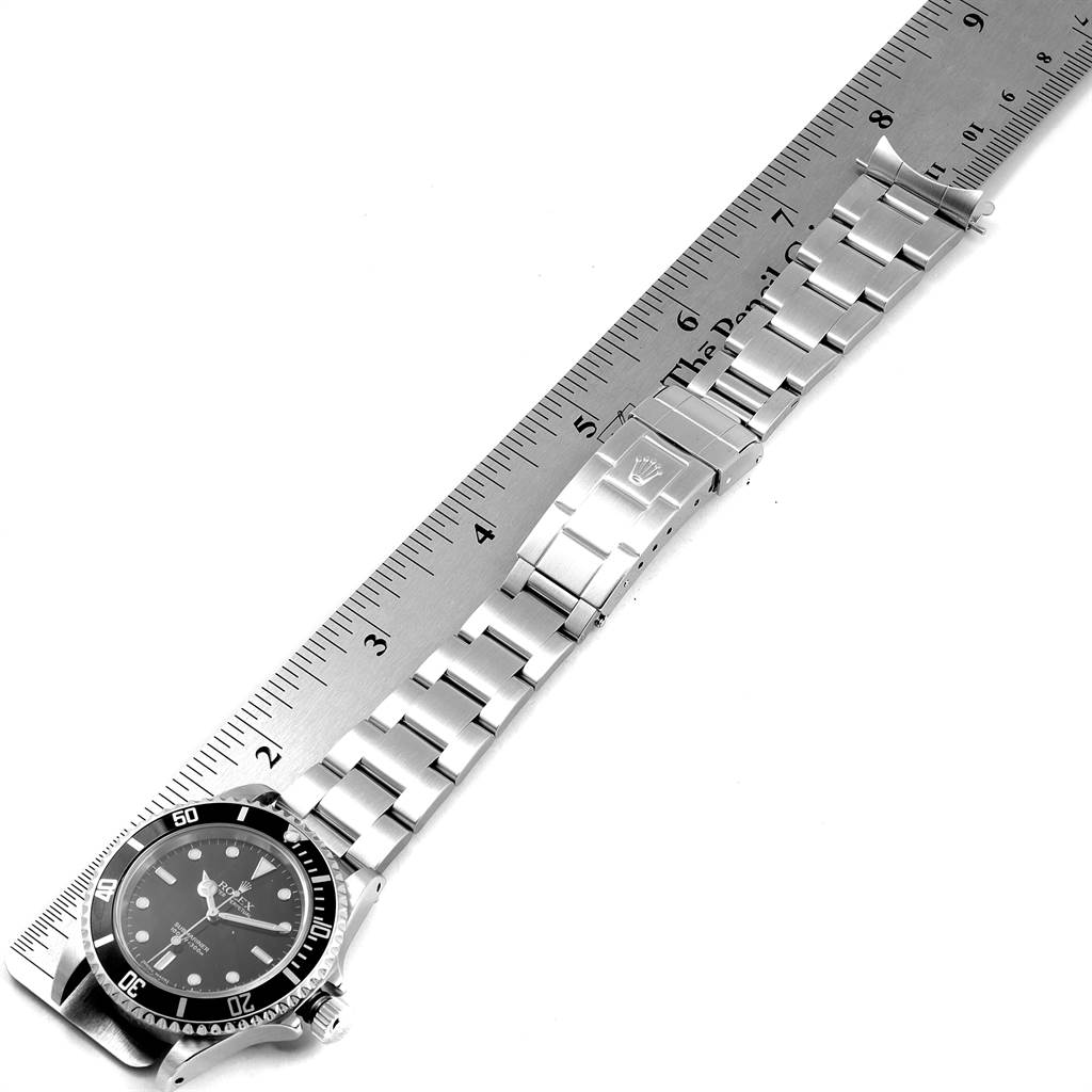 This image shows a Rolex Submariner 14060 Men
s Stainless Steel Black Dial 14060 Men
s Stainless Steel Black Dial watch laid flat next to a ruler, displaying the dial, bezel, and bracelet from a top-down angle.