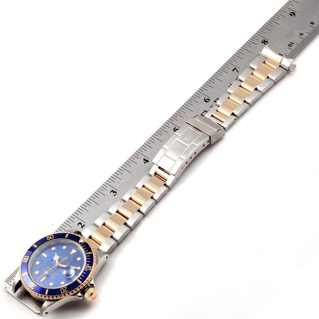 This image shows a top view of the Rolex Submariner 16613 Men
s Steel and Gold (two tone) Blue Dial 16613 Men
s Steel and Gold (two tone) Blue Dial watch, highlighting its face, bezel, and bracelet laying flat on a measuring scale.