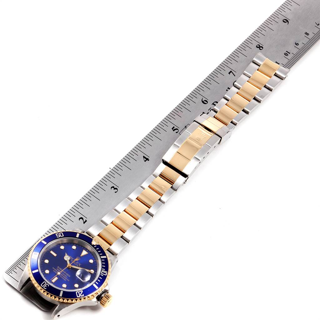 This image shows a Rolex Submariner 16613 Men
s Steel and Gold (two tone) Blue Dial 16613 Men
s Steel and Gold (two tone) Blue Dial watch laid flat with the band extended alongside a ruler for measurement.