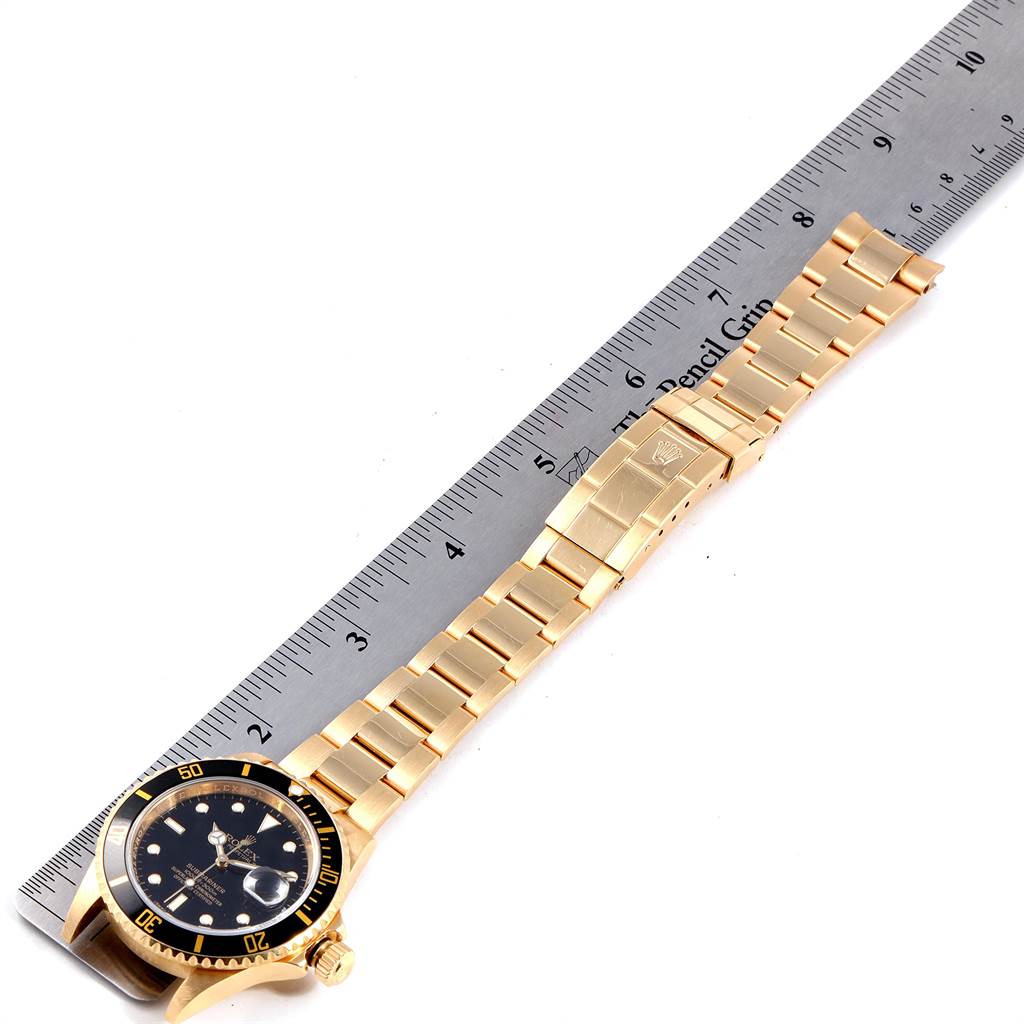 The image shows a Rolex Submariner 16618 Men
s Yellow Gold Black Dial 16618 Men
s Yellow Gold Black Dial watch laid flat with its face, bezel, crown, and bracelet clearly visible alongside a ruler for size reference.