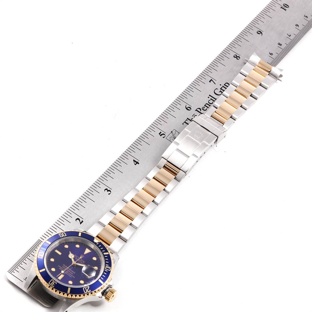 The image shows a Rolex Submariner 16613 Men
s Steel and Gold (two tone) Blue Dial 16613 Men
s Steel and Gold (two tone) Blue Dial watch laid flat, with a ruler positioned alongside the metal bracelet for measurement.
