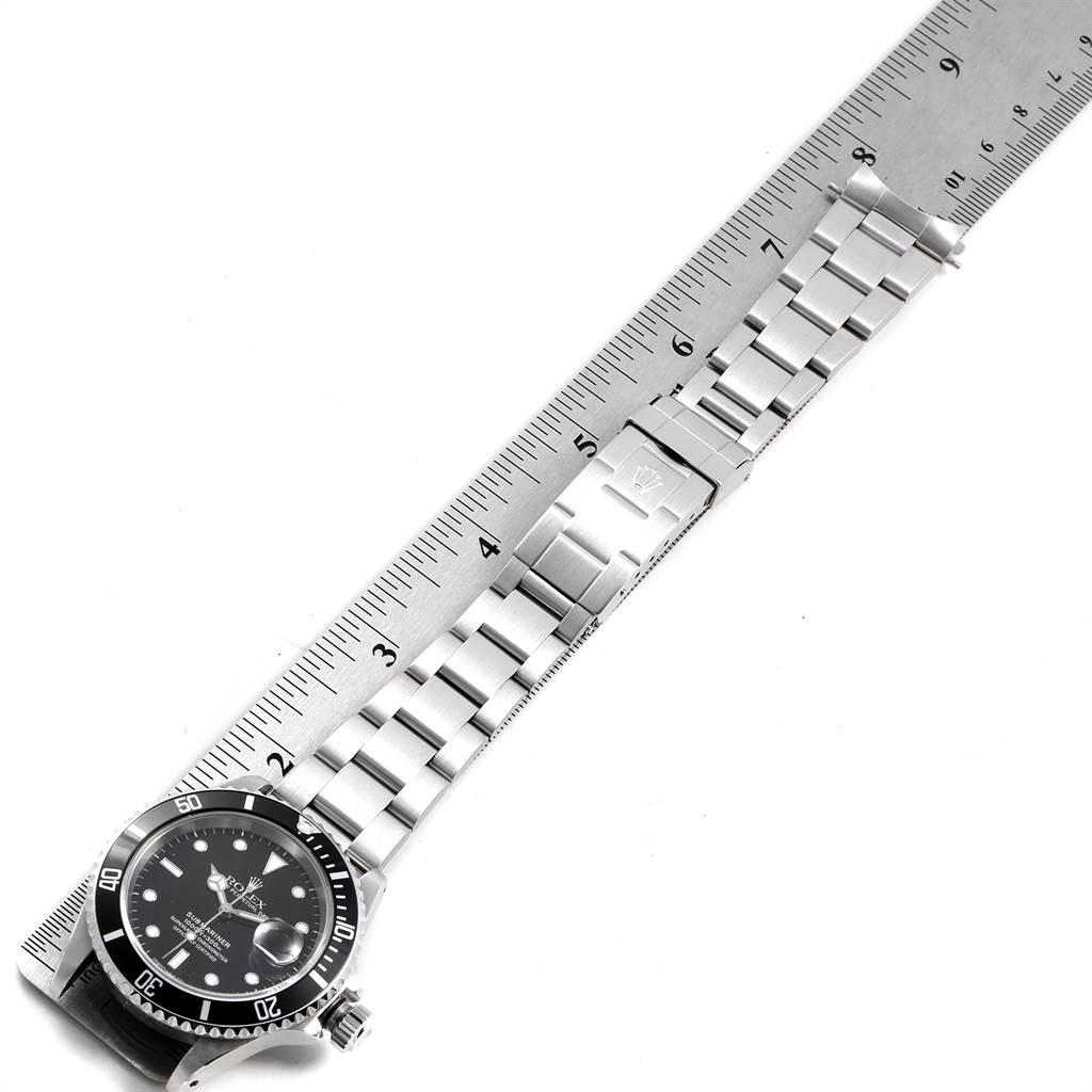 The image shows a Rolex Submariner 16610 Men
s Stainless Steel Black Dial 16610 Men
s Stainless Steel Black Dial watch with a detailed view of the face, bezel, and bracelet laid alongside a ruler for scale.