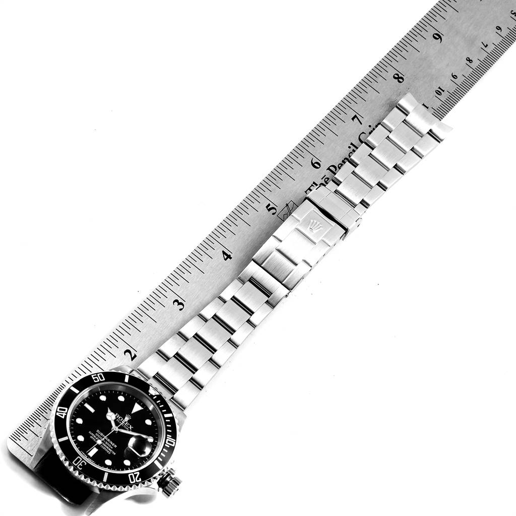 The image shows a top view of a Rolex Submariner 16610 Men
s Stainless Steel Black Dial 16610 Men
s Stainless Steel Black Dial watch, including its bezel, dial, bracelet, and clasp, measured against a ruler.