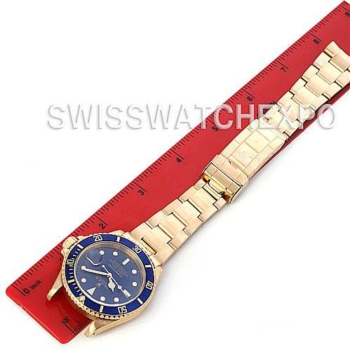 The Rolex Submariner 16618 Men's Stainless Steel Blue Dial 16618 Men's Stainless Steel Blue Dial watch is shown from an overhead angle, displaying its blue dial, bezel, and full bracelet alongside a red ruler.