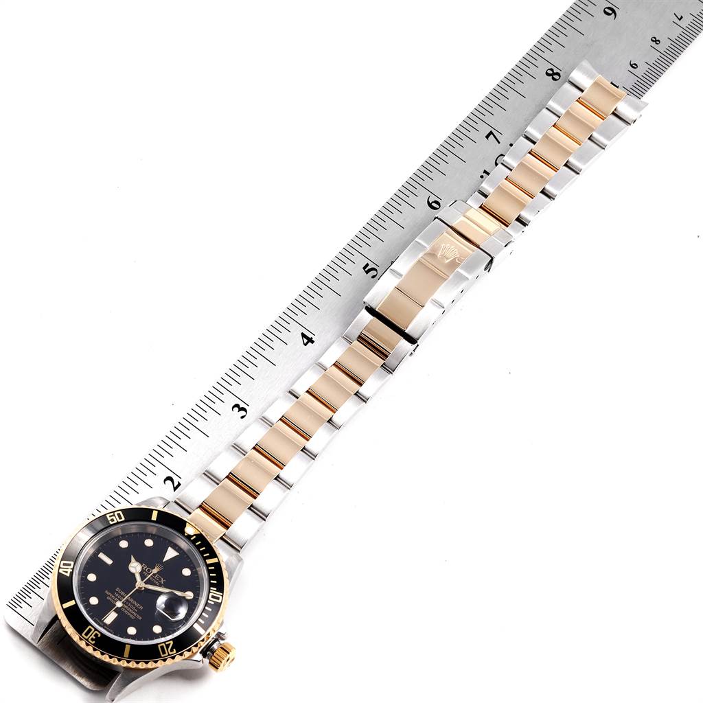 The image shows a top-down view of a Rolex Submariner 16613 Men
s Steel and Gold (two tone) Black Dial 16613 Men
s Steel and Gold (two tone) Black Dial watch with its band extended alongside a ruler.