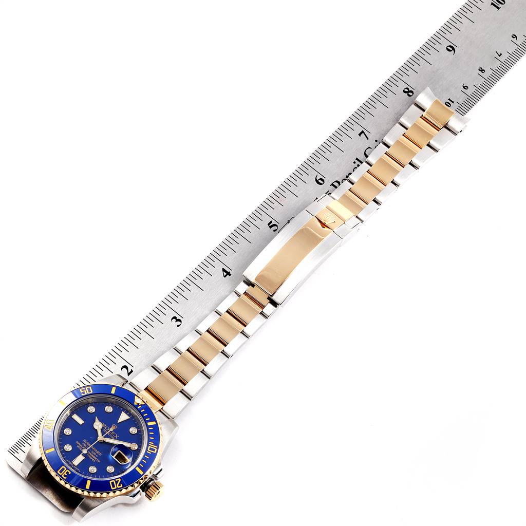 This image shows a top view of a Rolex Submariner 116613 Men
s Steel and Gold (two tone) Blue Dial 116613 Men
s Steel and Gold (two tone) Blue Dial
s blue and gold dial and band next to a ruler for size reference.