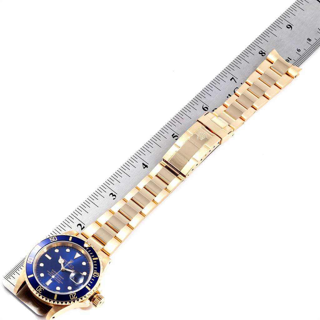 The image shows a Rolex Submariner 16618 Men's Yellow Gold Blue Dial 16618 Men's Yellow Gold Blue Dial model watch with a gold bracelet and blue dial, laid flat next to a ruler.