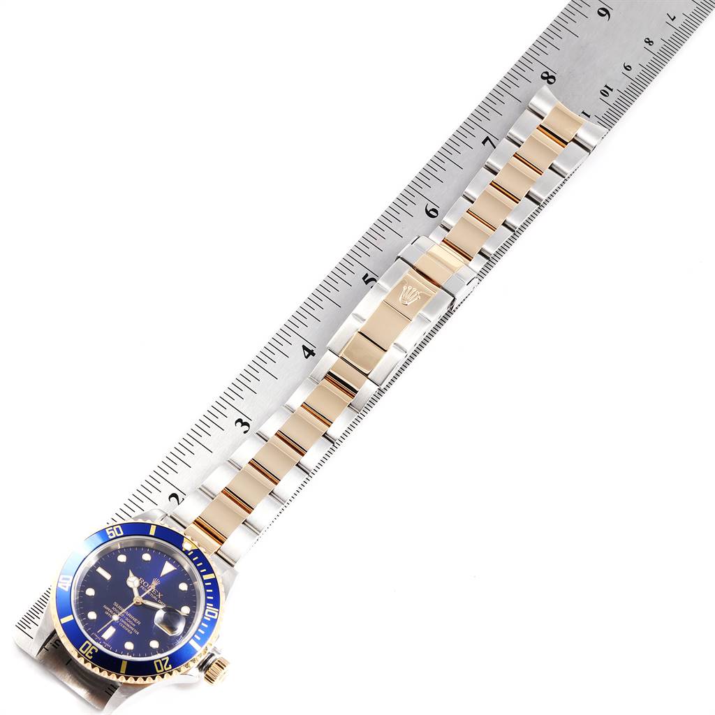 The Rolex Submariner 16613 Men's Steel and Gold (two tone) Blue Dial 16613 Men's Steel and Gold (two tone) Blue Dial watch is shown from a top-down angle, measured against a ruler to display its size, highlighting the bracelet and dial.