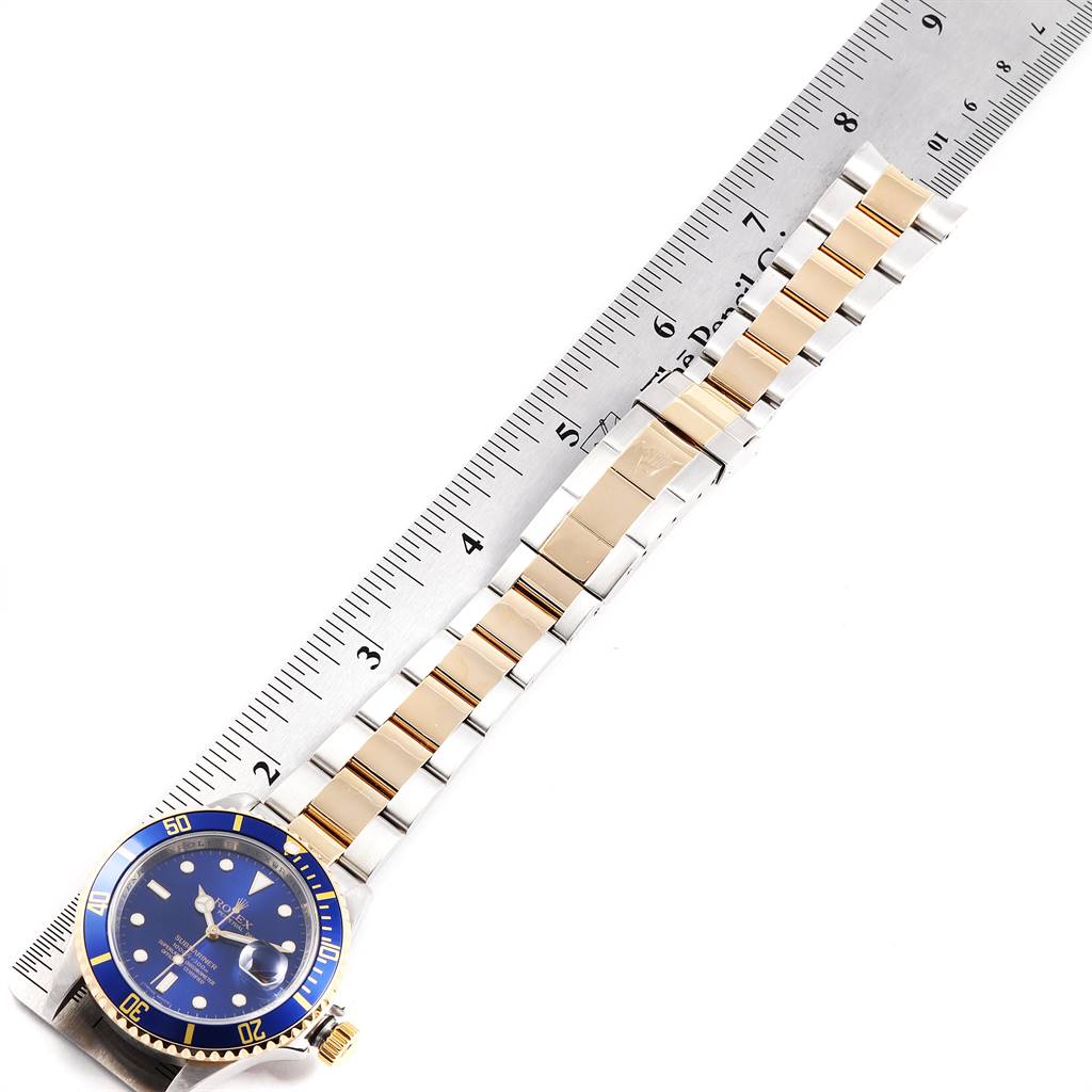 The image shows a Rolex Submariner 16613 Men
s Steel and Gold (two tone) Blue Dial 16613 Men
s Steel and Gold (two tone) Blue Dial watch laid flat, with the bracelet next to a ruler for size reference.