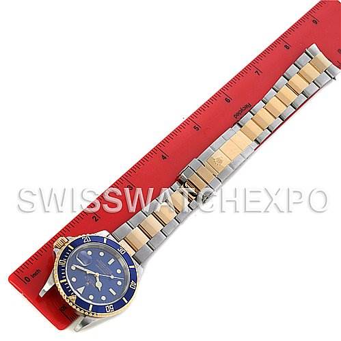 The image shows a full-length view of a Rolex Submariner 16613 Men's Yellow Gold Blue Dial 16613 Men's Yellow Gold Blue Dial watch with a blue dial and two-tone bracelet, laid beside a red ruler.