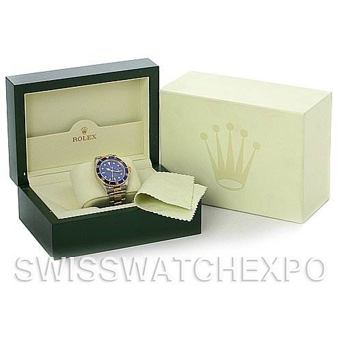 This image shows a Rolex Submariner 16613 Men's Yellow Gold Blue Dial 16613 Men's Yellow Gold Blue Dial watch in its open box, accompanied by a cleaning cloth and an outer box with the Rolex logo.