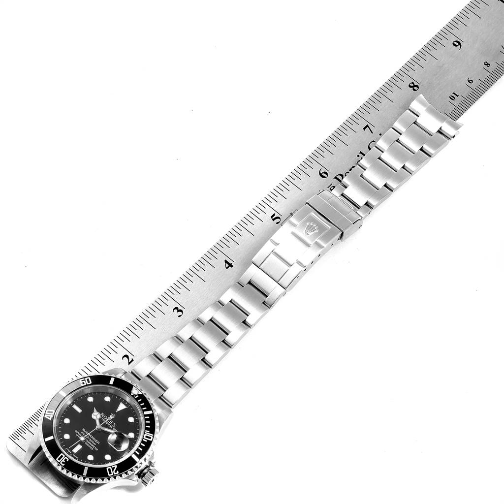 The image shows a Rolex Submariner 16610 Men
s Stainless Steel Black Dial 16610 Men
s Stainless Steel Black Dial watch laid flat alongside a ruler, displaying the face, bezel, and bracelet of the watch.