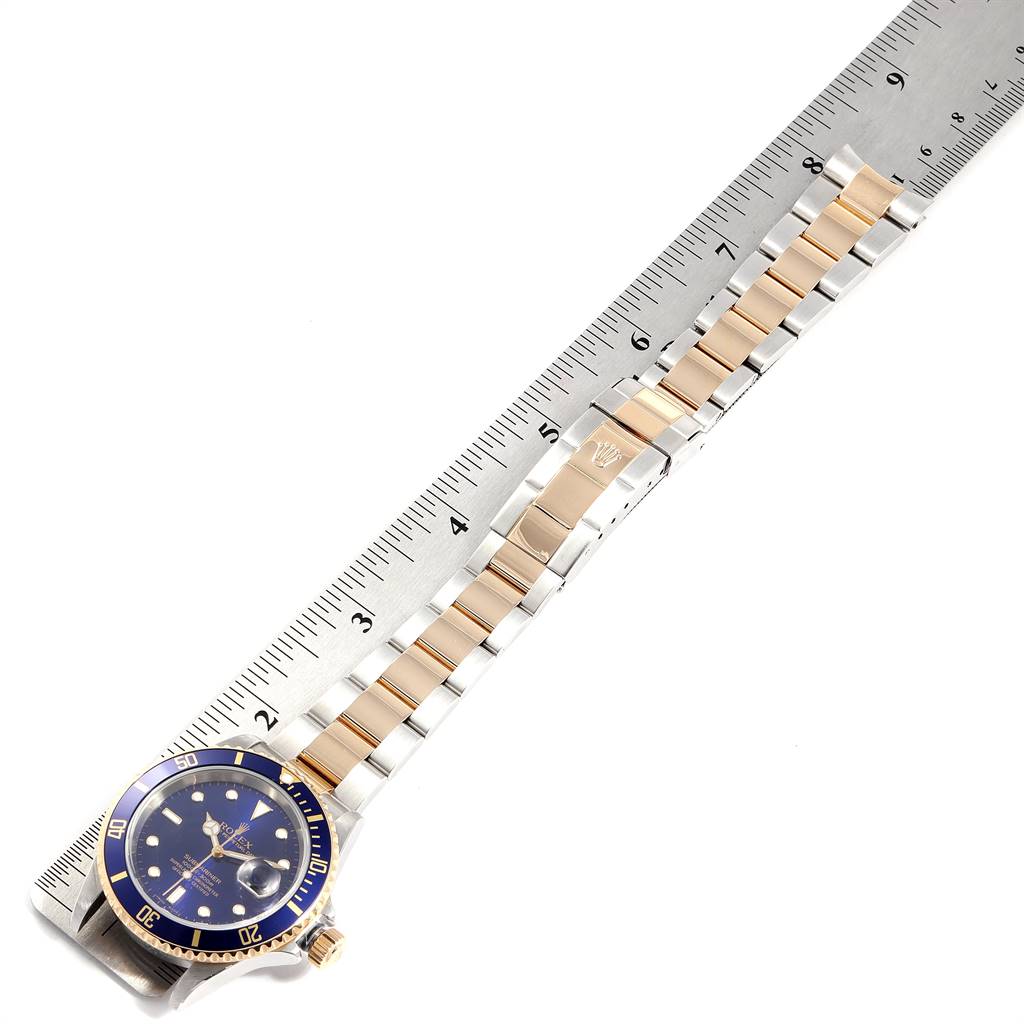 The image shows a top-down view of a Rolex Submariner 16613 Men
s Steel and Gold (two tone) Blue Dial 16613 Men
s Steel and Gold (two tone) Blue Dial watch on a ruler, highlighting the watch face and bracelet.