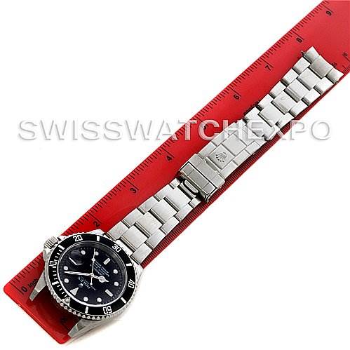 This Rolex Submariner 16610 Men's Stainless Steel Black Dial 16610 Men's Stainless Steel Black Dial watch is displayed flat alongside a red ruler, showing its entire bracelet and face.