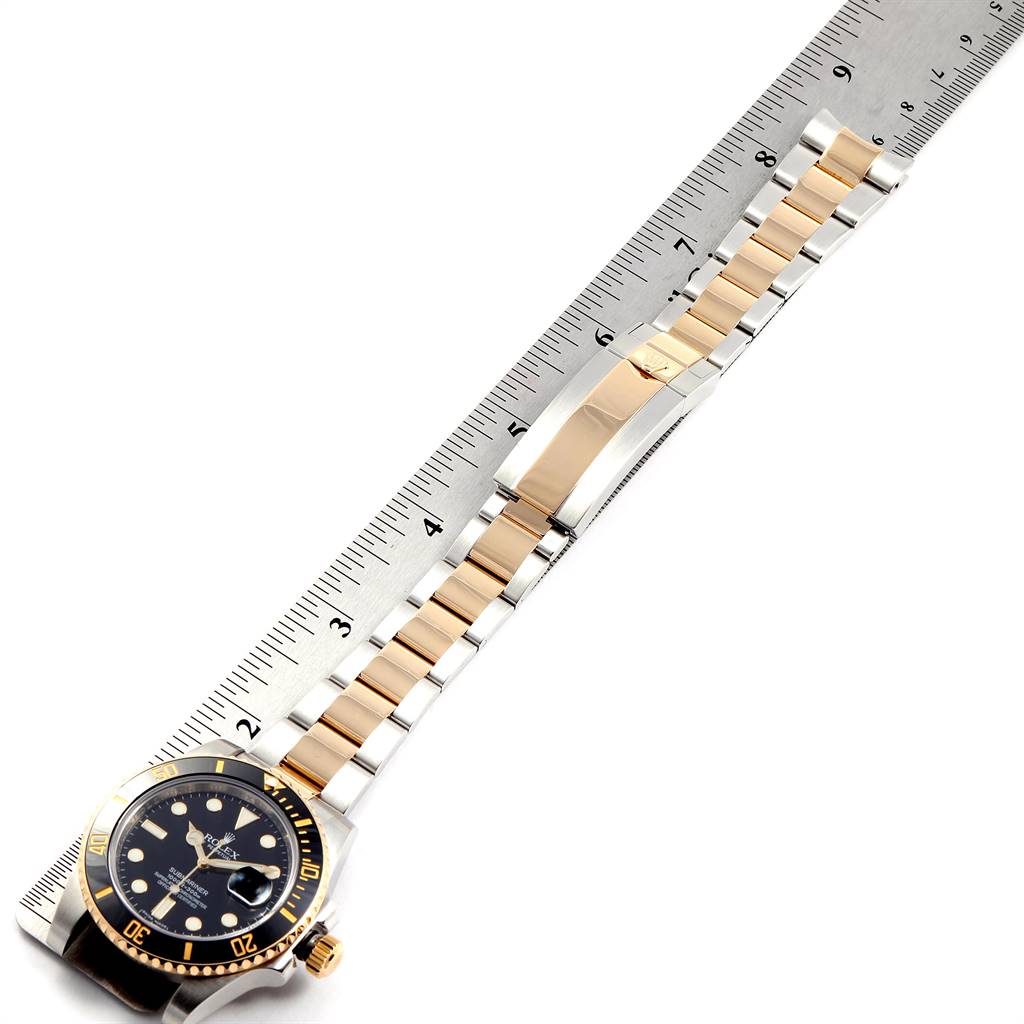 The image shows a top-down view of a Rolex Submariner 116613 Men
s Steel and Gold (two tone) Black Dial 116613 Men
s Steel and Gold (two tone) Black Dial watch, highlighting the face, bezel, and two-tone bracelet beside a ruler.