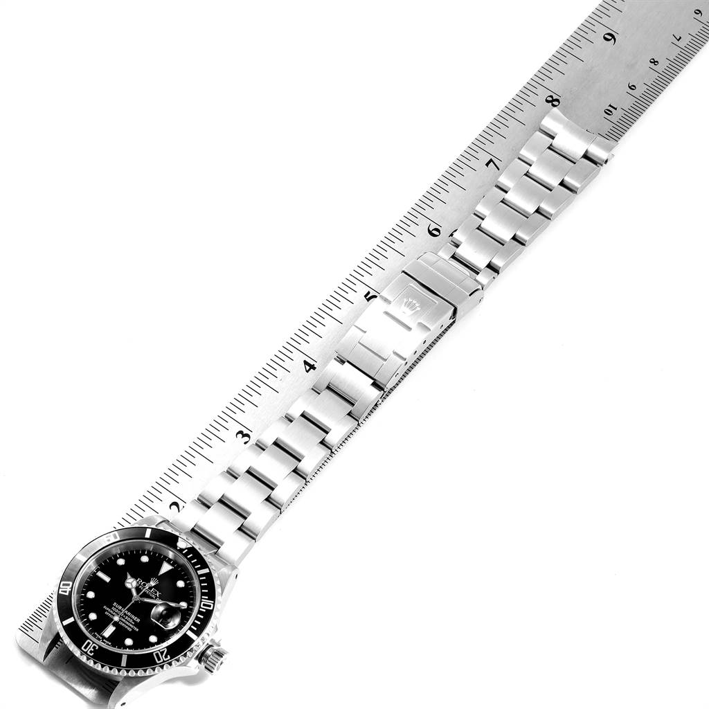 The image shows a top-down view of a Rolex Submariner 16610 Men
s Stainless Steel Black Dial 16610 Men
s Stainless Steel Black Dial watch, focusing on the dial and bracelet with a measuring ruler beside it.
