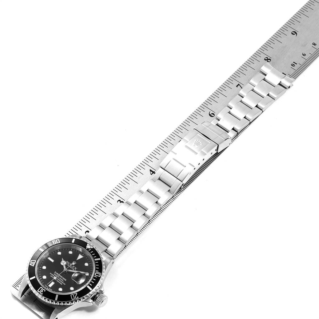 The image shows a Rolex Submariner 16610 Men
s Stainless Steel Black Dial 16610 Men
s Stainless Steel Black Dial watch laid flat against a ruler, highlighting the bracelet and clasp.