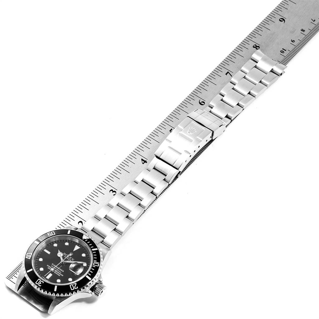 This image shows a top-down view of a Rolex Submariner 16610 Men
s Stainless Steel Black Dial 16610 Men
s Stainless Steel Black Dial watch with the strap alongside a ruler for measurement.