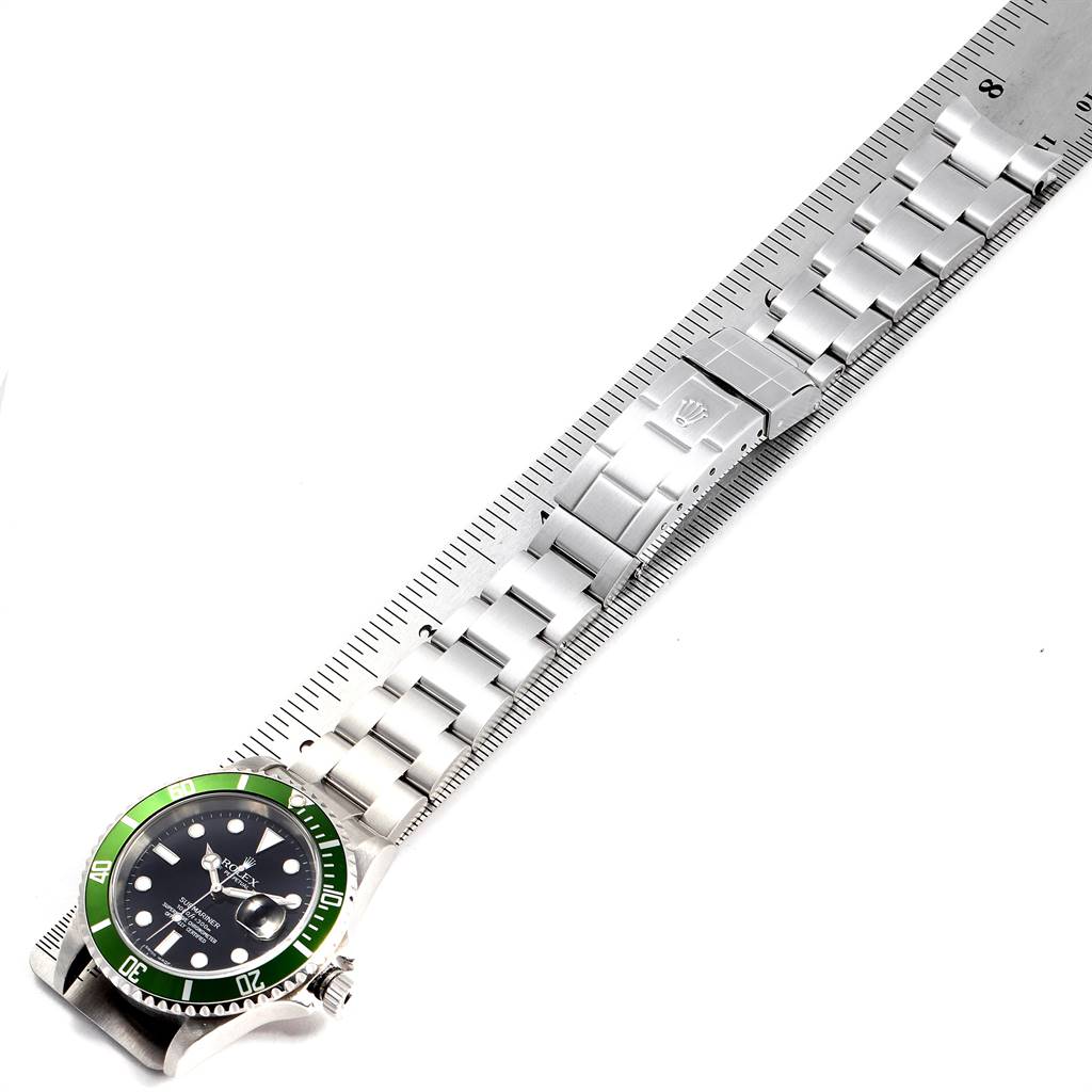 The image shows the front view of a Rolex Submariner 16610LV Men
s Stainless Steel Black Dial 16610LV Men
s Stainless Steel Black Dial watch with a green bezel and stainless steel band lying next to a ruler.