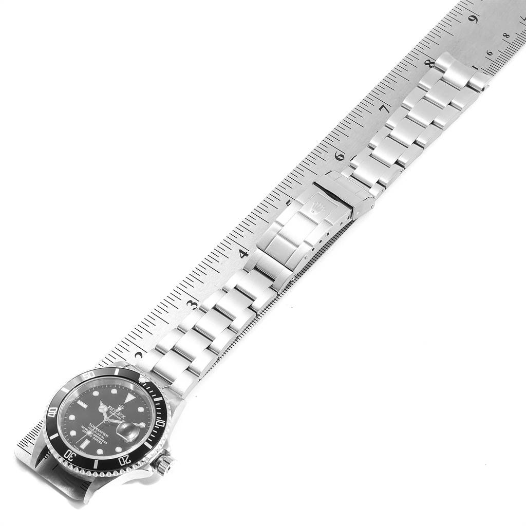 The image shows a Rolex Submariner 16610 Men
s Stainless Steel Black Dial 16610 Men
s Stainless Steel Black Dial watch laid flat alongside a ruler, displaying its face and metal bracelet.