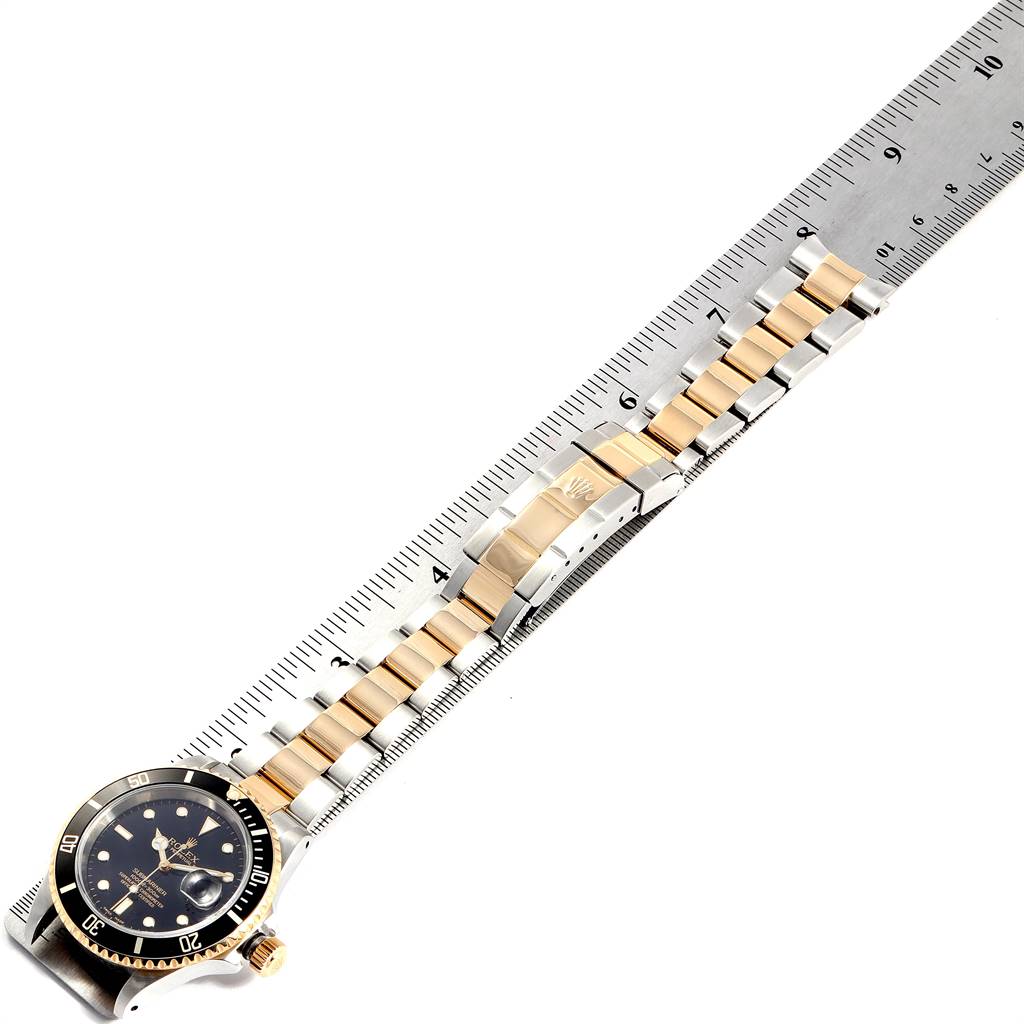 This image shows a top view of a Rolex Submariner 16613 Men's Steel and Gold (two tone) Black Dial 16613 Men's Steel and Gold (two tone) Black Dial watch laid next to a ruler, displaying the entire length of its band and black bezel.